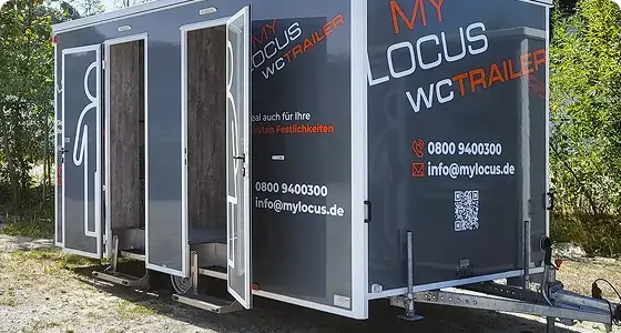 Schwarzer MY LOCUS WC-Trailer mit geöffneten Kabinentüren für getrennte Toiletten bei Veranstaltungen